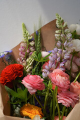 Close-up of a bouquet of colored flowers on a white background in kraft paper packaging with space for text. Ranunculus, lupine, flax and other flowers from the Ukrainian flower farm