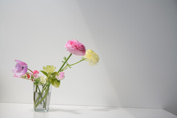 Delicate bouquet of different seasonal flowers of spring colors on white table on a white wall