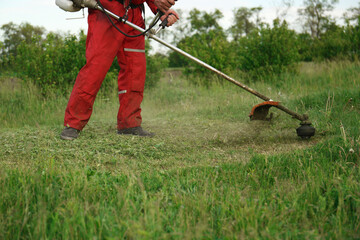 Worker cutting grass with string trimmer outdoors, closeup view