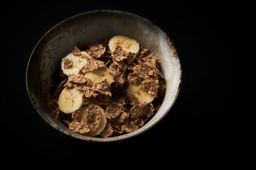 Bowl of granola with banana. Dark stone background. Close up. Copy space.