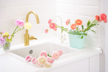 Beautiful white kitchen sink with pink fresh flowers and golden faucet