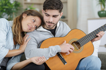 Fototapeta premium couple sitting and embracing on couch while man playing guitar