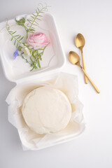 Small elegant white icing cake on packages with fresh flowers decor. Top view of beautiful tiny cake for two person.