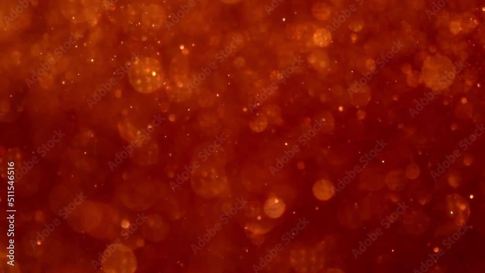 Sticker golden particles movement in red liquid. gold dust particles and bokeh moving slowly in red fluid. a