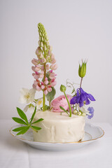 White cake with fresh lupine flowers, on a light background on a white plate. Wedding white cake with flowers