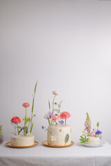 Fresh vegan cakes with white cream decorated with different fresh flowers in bright colors, on a light background with space for text