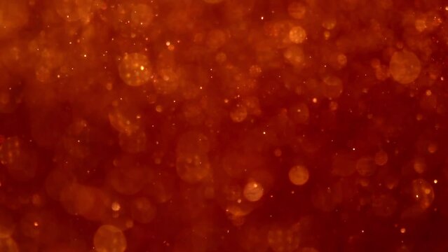 Golden Particles Movement In Red liquid. Gold dust particles and bokeh moving slowly in red fluid. Abstract relaxing background. 