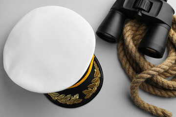 Peaked cap, rope and binoculars on light grey background, flat lay