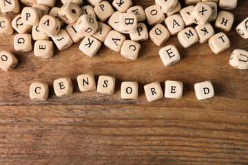 Small cubes with word Censored on wooden table, flat lay