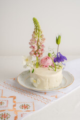 Obraz na płótnie Canvas White cake with fresh lupine flowers, on a light background