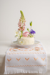 Elite wedding cake with a mix of fresh flowers with lupine, on a light background with local confectionery. Vegan wedding white cake