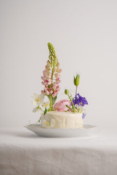 White cake for one person, decorated with flowers with lupine and other colored flowers
