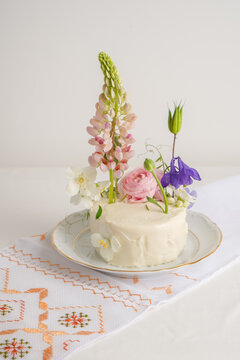 White cake with fresh lupine flowers, on a light background
