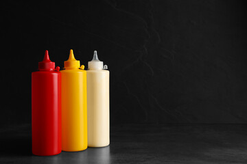 Ketchup, mustard and mayonnaise in squeeze bottles on grey table, space for text