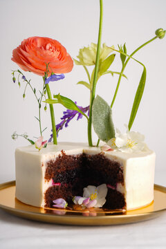 Close-up of a cake with flowers with a chocolate cut on a golden plate on a white table