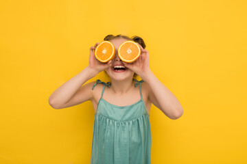a happy girl in summer clothes holds orange pops in front of her eyes on a yellow background, a smiling girl made binoculars from oranges