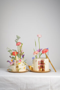 Creative composition with a cake, a slice of dessert and golden utensils, a cake with white cream with different fresh flowers, on a white background. Wedding fashion for desserts