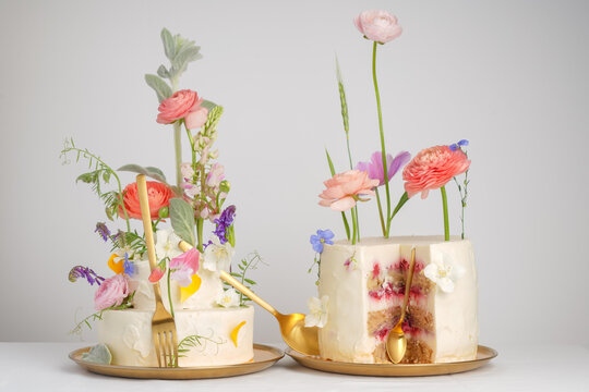 Creative composition with a sweet table, a cake with white cream with different fresh flowers, on a white background. Wedding fashion for desserts