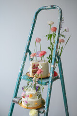 Holiday after renovation. Different cakes with berries inside and fresh flowers on a light background on a golden plate on the stairs ladder. Beautiful cake with flowers on a ladder after renovation