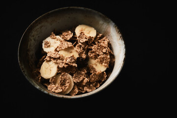 Bowl of granola with banana. Dark stone background. Close up. Copy space.