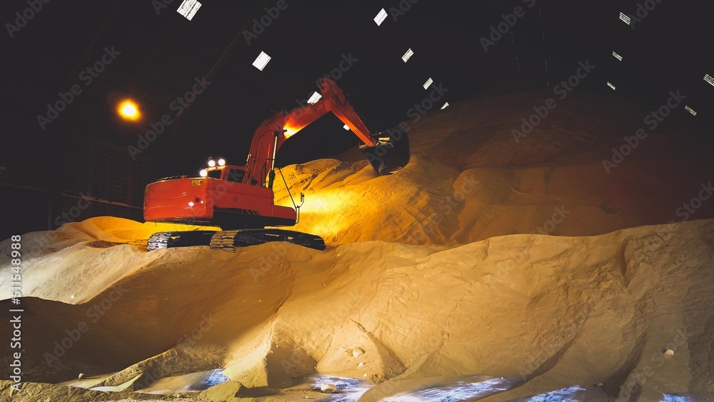 Wall mural excavator, backhoe standing on pile of raw brown sugar inside a warehouse, bulk sugar handling, and 