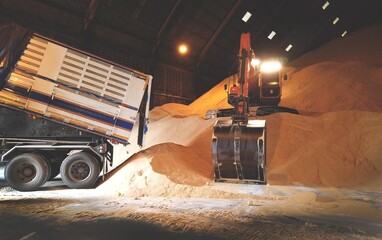 Excavator, Backhoe unloading raw brown sugar inside huge warehouse. Bulk sugar handling, and...