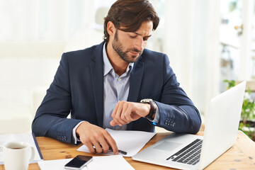Keeping an eye on the time. A handsome businessman checking the time on his watch at his desk.