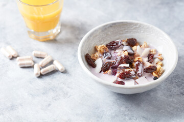 Bowl of granola with yogurt, nuts, cranberry and cocoanut. Sport supplements ( carnitine capsules ) in background. Bright stone  background. Close up. Copy space. 