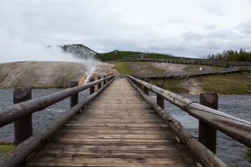 Fototapeta premium Bridge across river around Hot spring Geyser in American Landscape. Yellowstone National Park, Wyoming, United States. Nature Background.