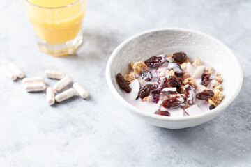  Bowl of granola with yogurt, nuts, cranberry and cocoanut. Sport supplements ( carnitine capsules ) in background. Bright stone background. Close up. Copy space.