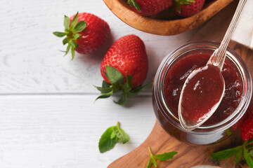 Strawberry jam. Strawberry jam in glass jar with fresh berries plate on white wooden table background, closeup. Homemade strawberry fruity jam. Top view with copy space.