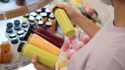 A woman customer in a store chooses bottles of freshly squeezed juice from different fruits and...