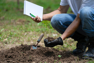 specialist one hand  checking quality of soil before planting and other hand holding notebook and pen. concept soil improvement for agriculture