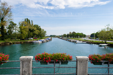 Un canale del porticciolo di Grado visto da un ponte con le fioriere, lungo la Via Flavia, cammino...