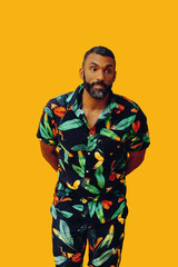 handsome mid adult bearded african american man wearing Hawaiian shirt and shorts on yellow...
