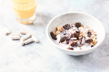 Bowl of granola with yogurt, nuts, cranberry and cocoanut. Sport supplements ( carnitine capsules ) in background. Bright stone background. Close up. Copy space.