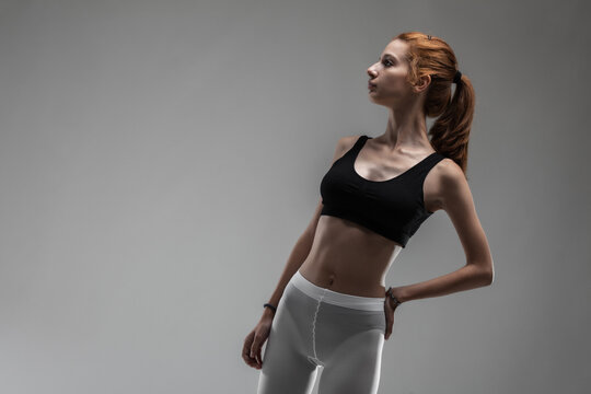 Fit girl with black top and white leggings posing against gray background...