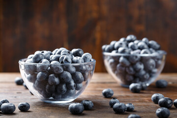 Freshly picked blueberries in a glass bowl on a wooden background. Healthy food and nutrition concept.