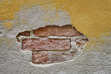 Mur jaune ancien avec enduit manquant et briques apparentes.