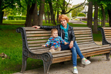 beautiful girl (mother) with a boy (son) in the park in the park are sitting on a bench