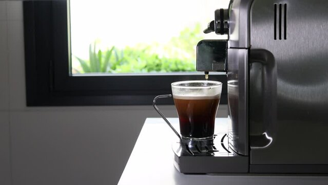 Coffemaker finishing pouring a coffe in a glass cup. Kitchen interior at home.