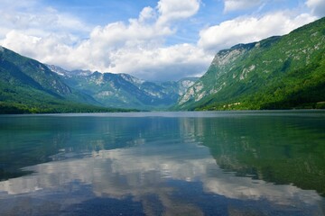 Fototapeta na wymiar View of Bohinj lake surrounded by mountains in Julian alps and Triglav national park, Slovenia in summer and a reflection of the mountains and the clouds in the water