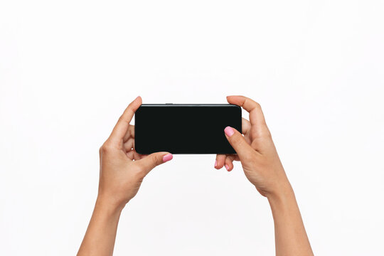 Mobile phone with black screen in female hands isolated on a white background. Blank with an empty copy space for the text. Template for the design. Mockup of a smartphone. A young woman takes picture