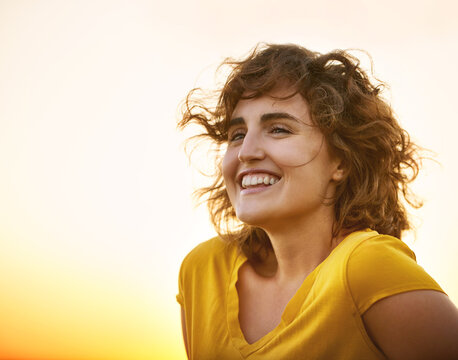 Shes got sunshine in her soul. Shot of a cheerful young woman smiling while standing outside at sunset.