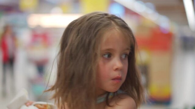 Child sitting shopping cart in store store eats tasty roll churras. Quick snack for children. Backing snack for kids. Little cute girl bites sweet bun and chews. Family in supermarket for buing