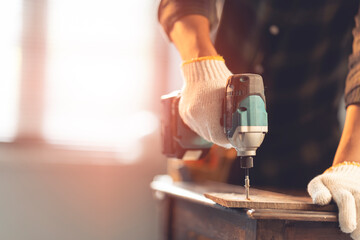 Male mechanic using a cordless screwdriver drill with wood screws in the workshop. - obrazy, fototapety, plakaty