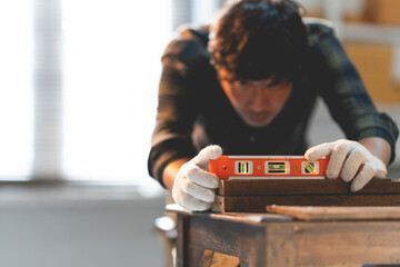 A male craftsman is using a wooden spirit level in his workshop. - obrazy, fototapety, plakaty