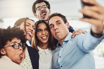 Try and look serious guys. Shot of a group of cheerful work colleagues taking a self portrait together inside of the office during the day.