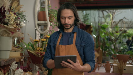Male employee checking inventory holding tablet standing inside flower shop. Small business store staff