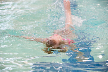 3 year old girl swimming in an indoor pool floating on her back